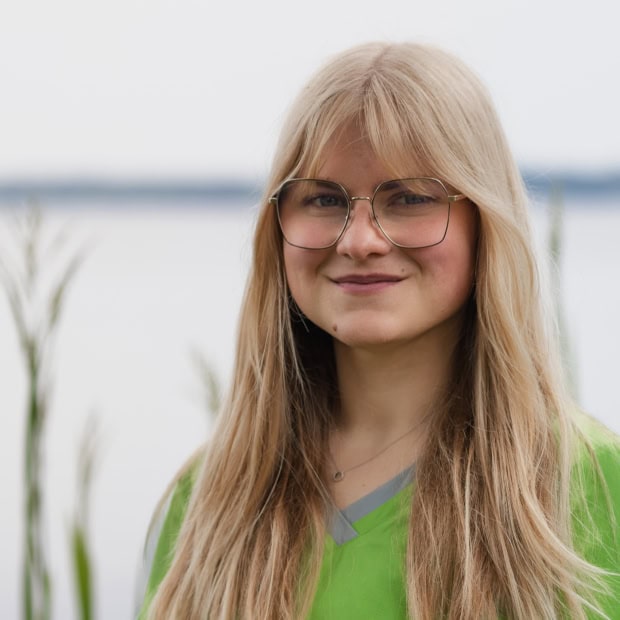04. Marie-Louise Rhode Junge Frau mit Brille vor Wasser und Natur im Hintergrund.