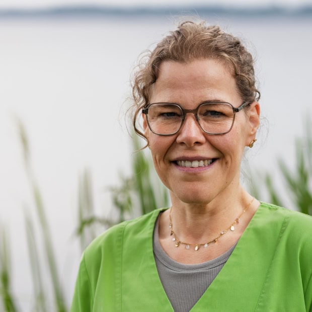 07. Marion Marmelo Ärztin im Grünen vor Wasser mit Pflanzen im Hintergrund.
