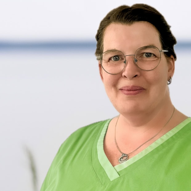 08. Nicole Wollgam Ärztin in grüner Praxisuniform mit Brille lächelnd.