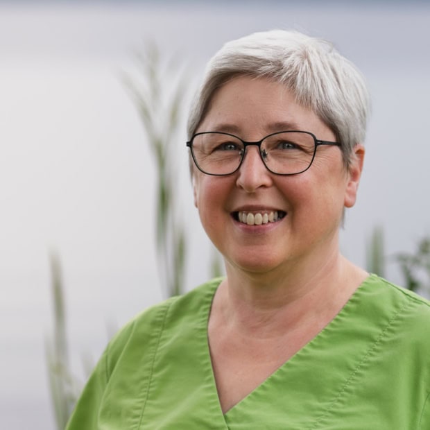 09. Renate Suter Ärztin in grüner Praxisuniform lächelnd vor Praxis am Glockenturm.