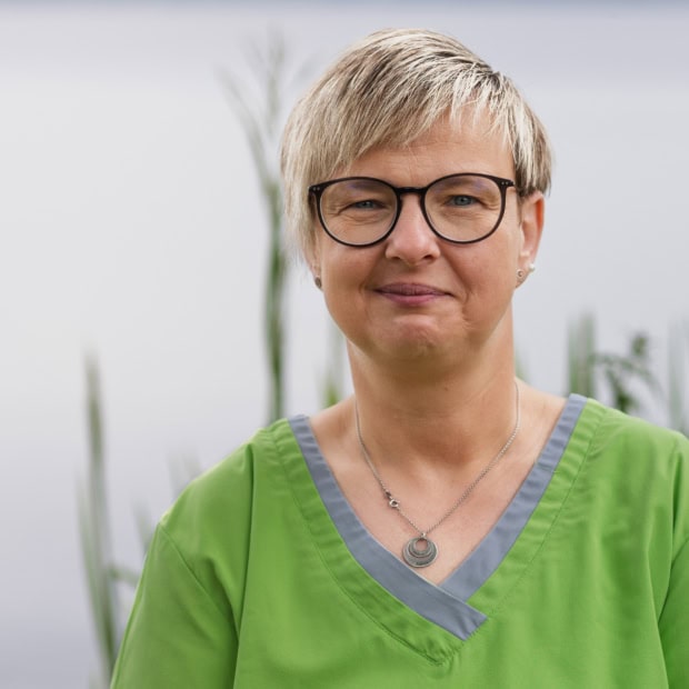 10. Sandra Bäker Ärztin in grüner Praxisuniform vor Praxis am Glockenturm.