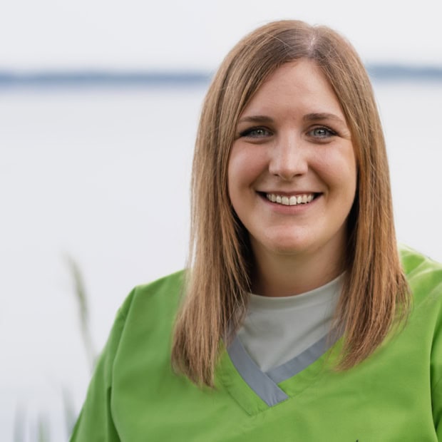 12. Stefanie Tholen Freundliche medizinische Fachkraft in grüner Uniform vor Wasserlandschaft.